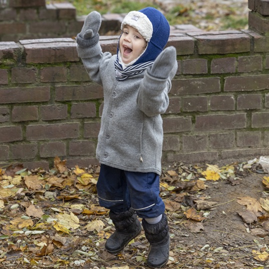 Hüpfender Junge mit Pickapooh-Wintermütze im Herbstlaub